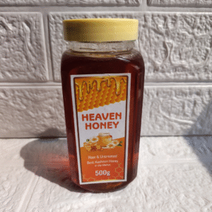 Heaven Honey brand jar of pure raw Acacia Honey, 500g, with a yellow cap, against a white textured wall.