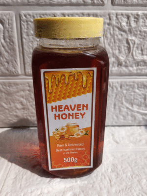 Heaven Honey brand jar of pure raw Acacia Honey, 500g, with a yellow cap, against a white textured wall.